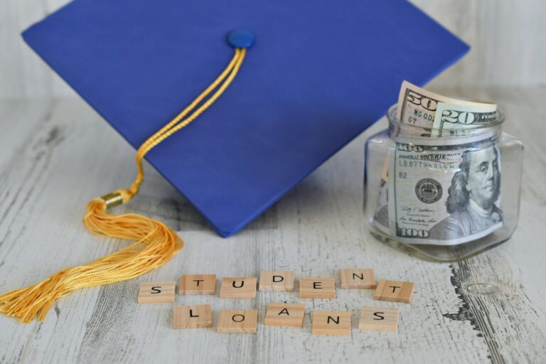 Graduation cap mortarboard with tassel propped on a jar of money cash, words STUDENT LOANS