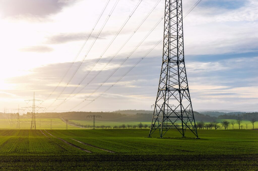 Scenic view of electricity pylons stretching across green fields warm sunset sky background